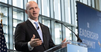 Heritage Foundation President Kevin Roberts, in a black suit with a blue tie, speaks in front of a backdrop reading 