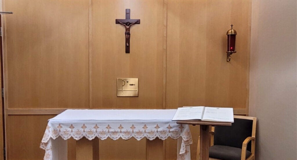 Glass-covered candle burns to the right of a crucifix in a chapel.