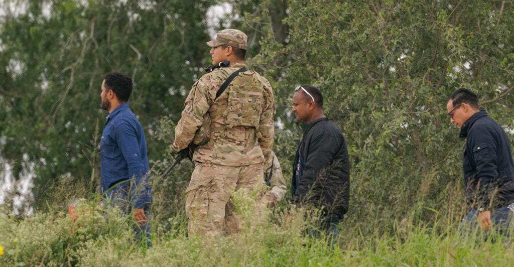 A National Guardsman escorts three male illegal aliens to Border Patrol outside.