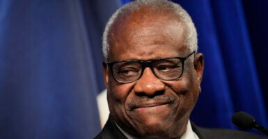 Clarence Thomas smiles in a suit in front of a blue background