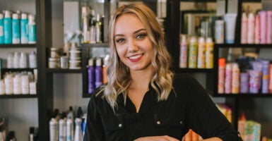 Young blonde hair stylist smiles in front of hair products