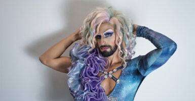A man is dressed in a dress while wearing makeup and a blonde wig