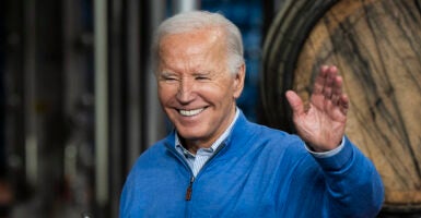 President Joe Biden waves in a blue sweatshirt in front of a beer barrel
