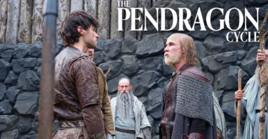 An elderly man with a beard and long hair beneath a bald spot stands in chain mail and armor confronting a young man with black hair in front of a rock wall. Text reading "The Pendragon Cycle" rests above their heads.
