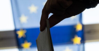 A woman's hand drops a paper ballot into a ballot box in front of the European Union flag.