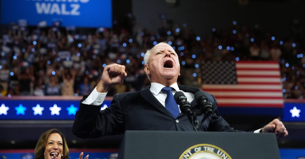 Walz pumps his fist and shouts as he stands at a podium.