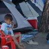 two small boys sitting outside in front of tents at a makeshift migrant shelter
