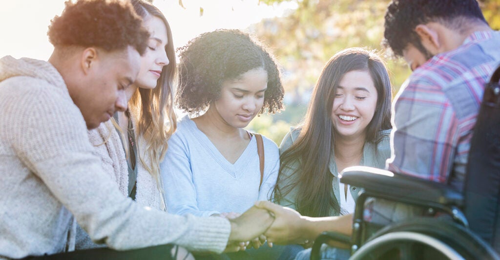 A diverse group of college friends hold hands and pray together on campus.