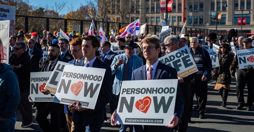 Pro-life protesters march down a street holding signs.