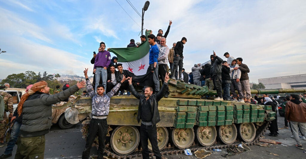 Syrians celebrate while standing on top of a military tank.