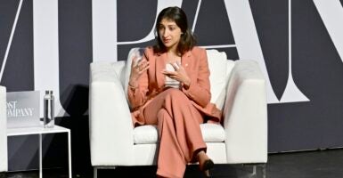 Lina Khan sits in a sofa couch seat with her legs crossed while speaking.