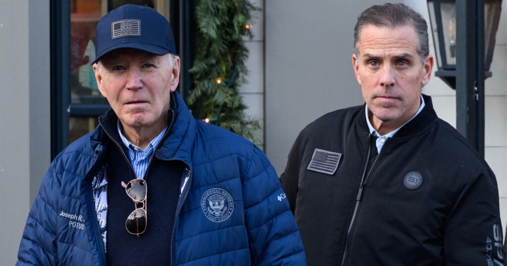 Joe Biden, wearing a navy blue baseball cap and matching winter coat, stands next to his son, Hunter Biden, who is wearing a black zip-up jacket.