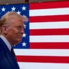 Donald Trump walks with Melania in front of a screen displaying with the United States flag.