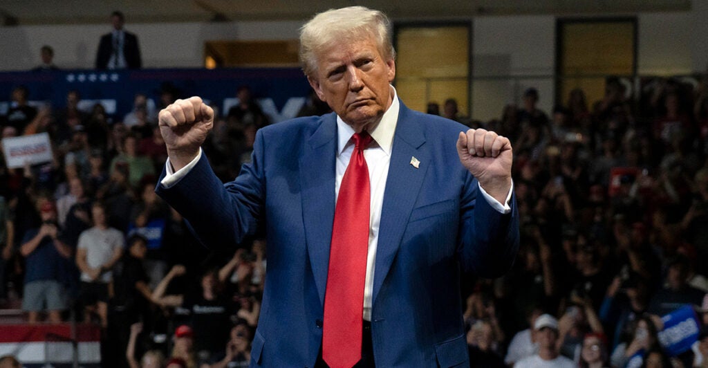 Donald Trump, in a navy suit and red tie, dances with his fists in the air on stage.
