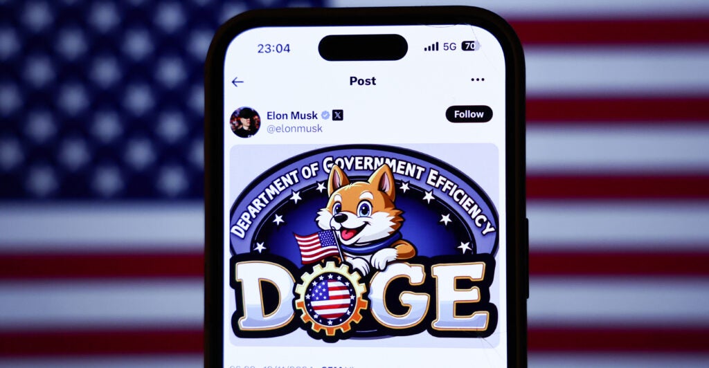 American flag displayed on a laptop screen and Elon Musk post about DOGE on X displayed on a phone screen