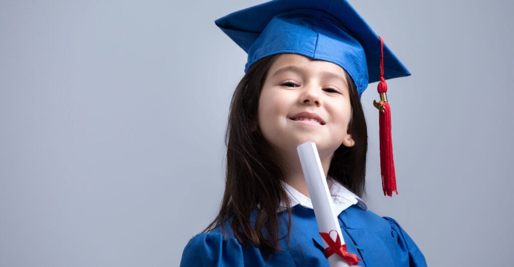 A young girl wearing a blue graduate-style cap and gown and holding a diploma