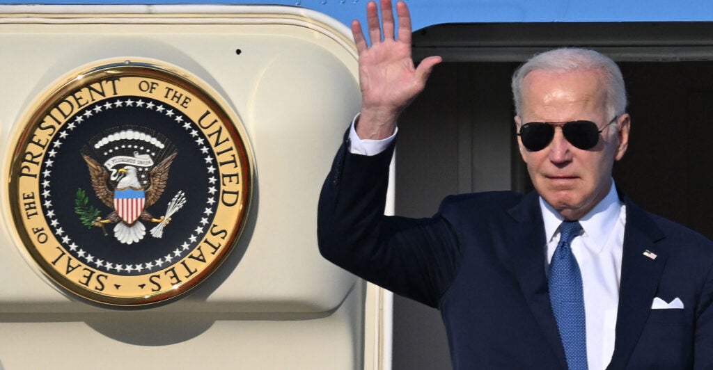 President Joe Biden waves at the door of Air Force One aas he disembarks. The official presidential seal is on the open door beside him.