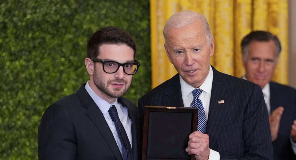Alex Soros stands next to then-President Joe Biden as Mitt Romney claps in the background