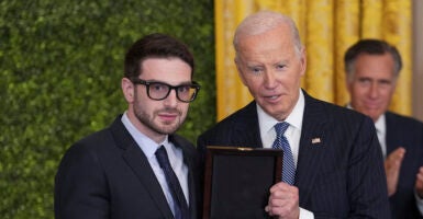 Alex Soros stands next to then-President Joe Biden as Mitt Romney claps in the background