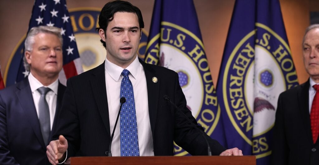 Brandon Gill stands at a podium wearing a suit with a blue tie.