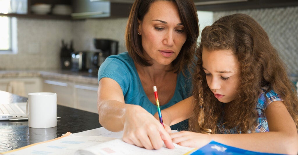 A mother helps her daughter with her homework in the family kitchen.