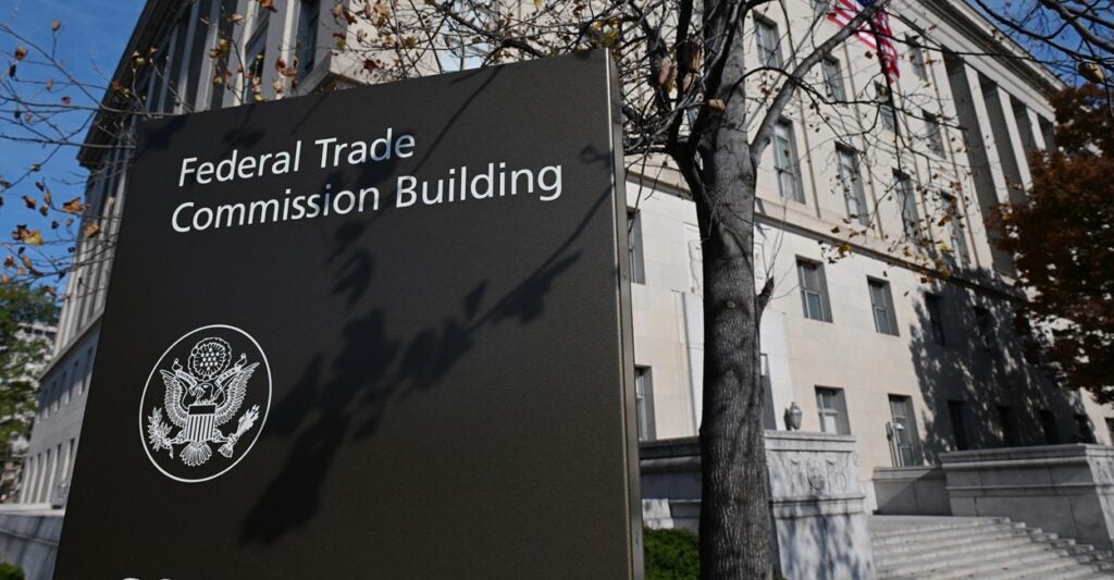 The Federal Trade Commission building stands behind a sign identifying it next to a tree.