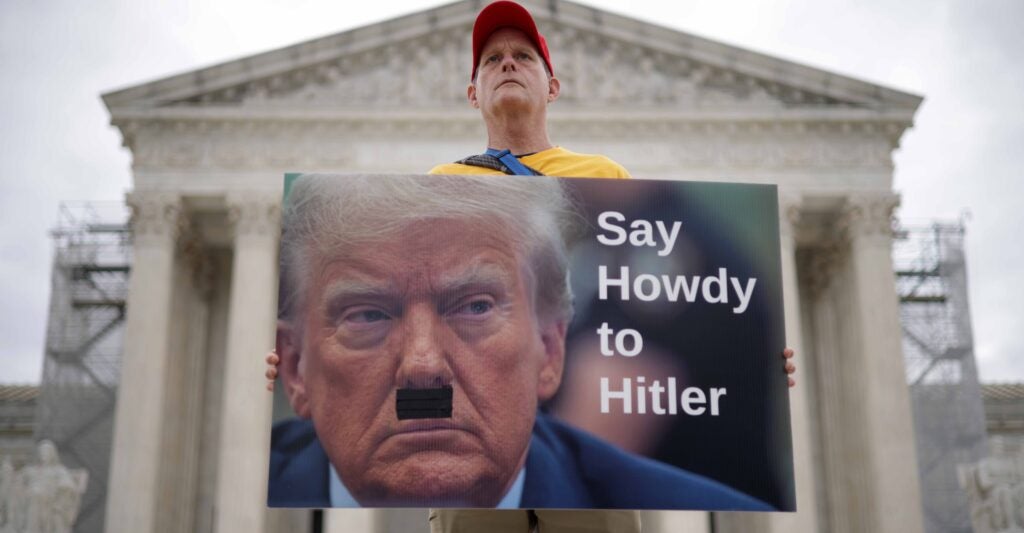 An anti-Trump fanatic holds a sign equating Donald Trump to Adolf Hitler in front of the Supreme Court.