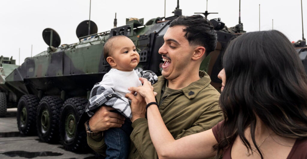 A military service member dressed in his green uniform holds his young son, who wears a white shirt and blue jeans.