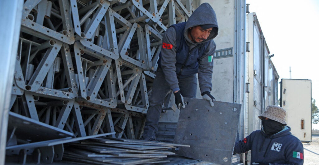 A man in a blue work suit wears a hood as he unloads equipment from a truck.