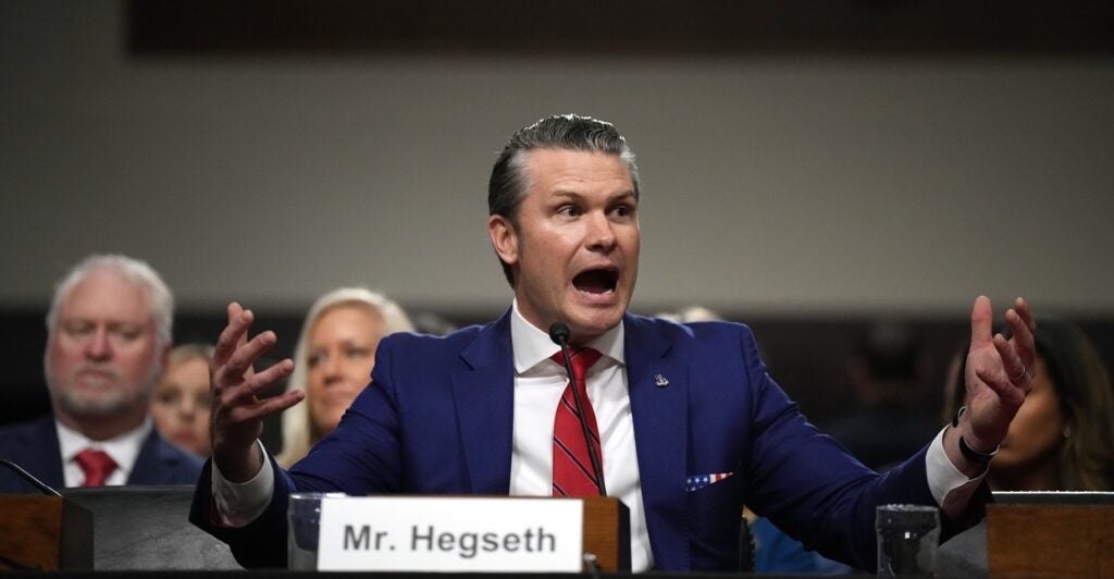 Pete Hegseth raises his arms and talks in an animated fashion during a Senate hearing