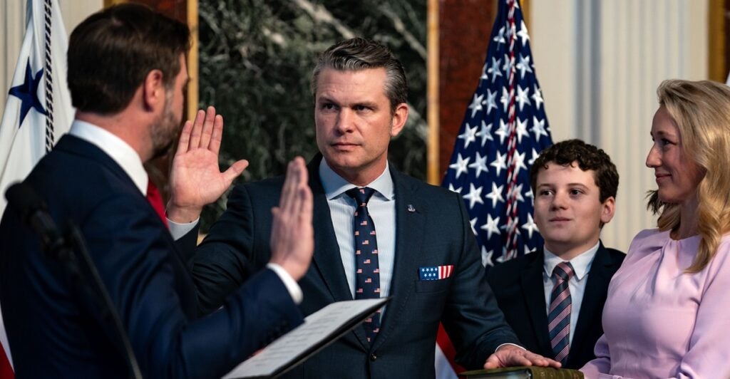 Pete Hegseth raises his right hand and puts his left hand on the Bible.