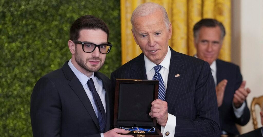 Alex Soros and Joe Biden both hold the Medal of Freedom while they pose for a photo.