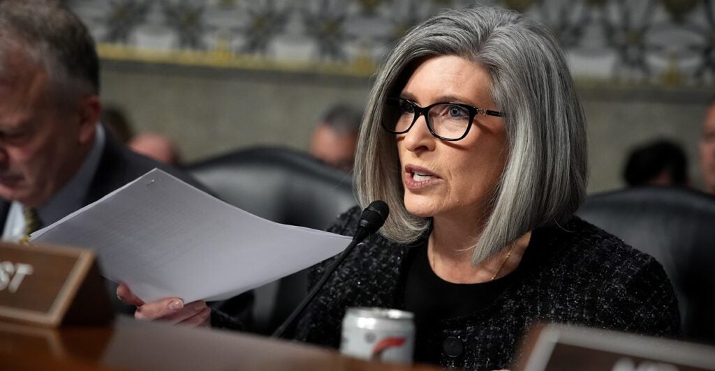 Joni Ernst sits at a table and speaks into a microphone.