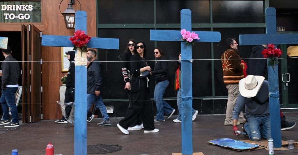 People walk by large crosses are on a sidewalk on Bourbon Street in New Orleans.