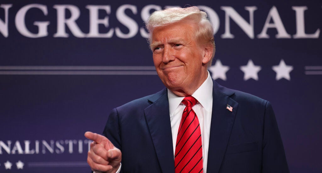 President Donald Trump points and smiles while wearing a blue suit with a red tie