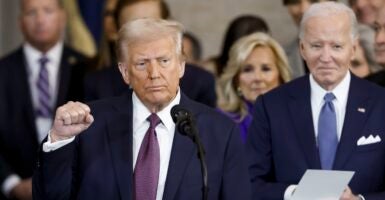 Donald Trump stands at a podium with his right hand raised in a fist.