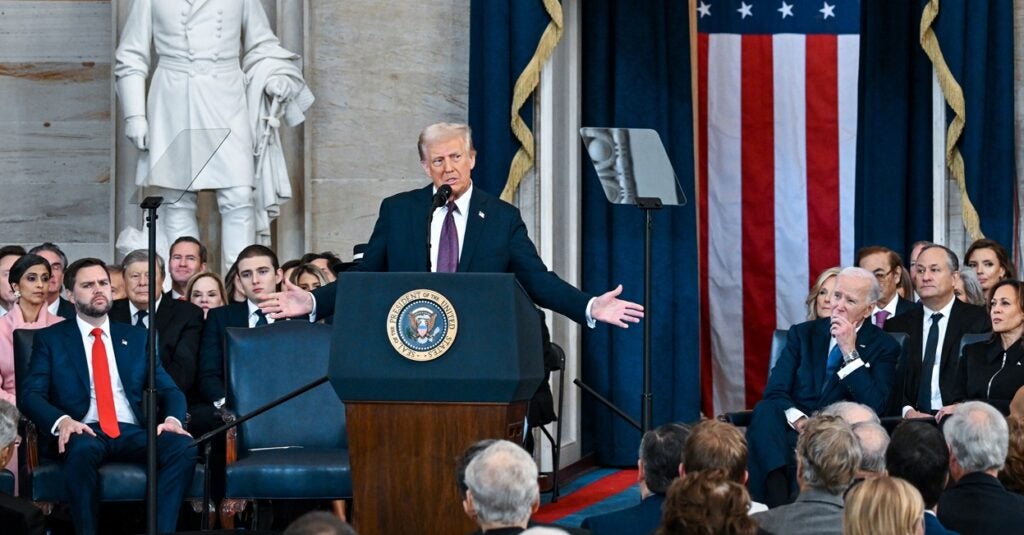 Donald Trump stands at a podium with his arms outstretched.