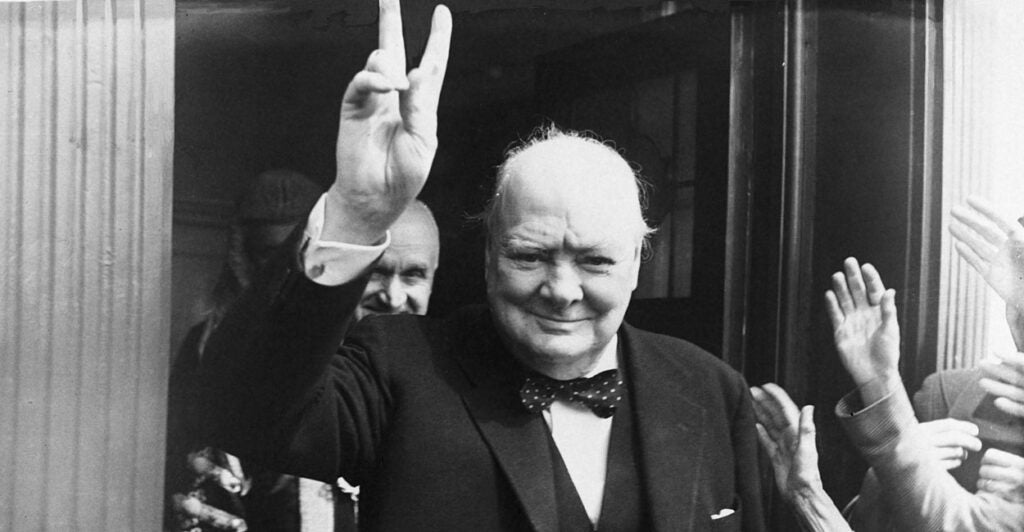 In a three-piece suit and bowtie, British Prime Minister Winston Churchill gives his famous wartime V-sign