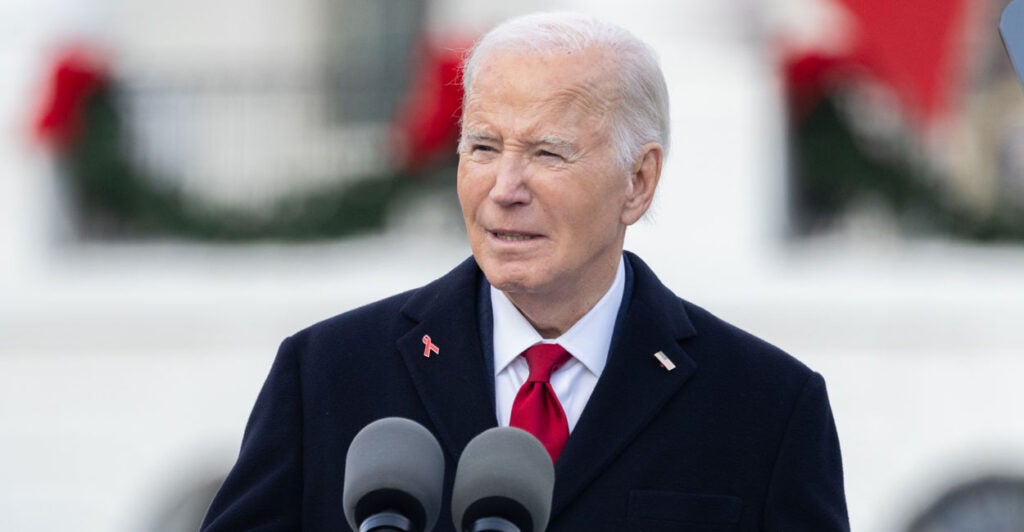 Joe Biden in a dark suit and jacket at a podium on the white house lawn