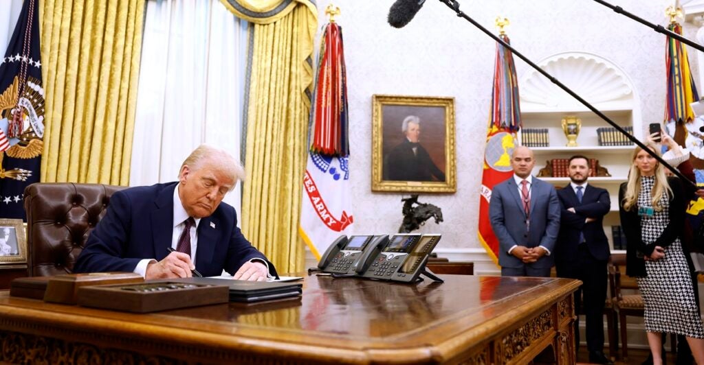 Donald Trump sits at his desk signing an executive order.