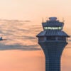 An aircraft approaches an air traffic control tower as it comes in for a landing at sunset.