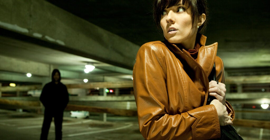Woman in a parking garage looks over her shoulder nervously at a possible stalker.