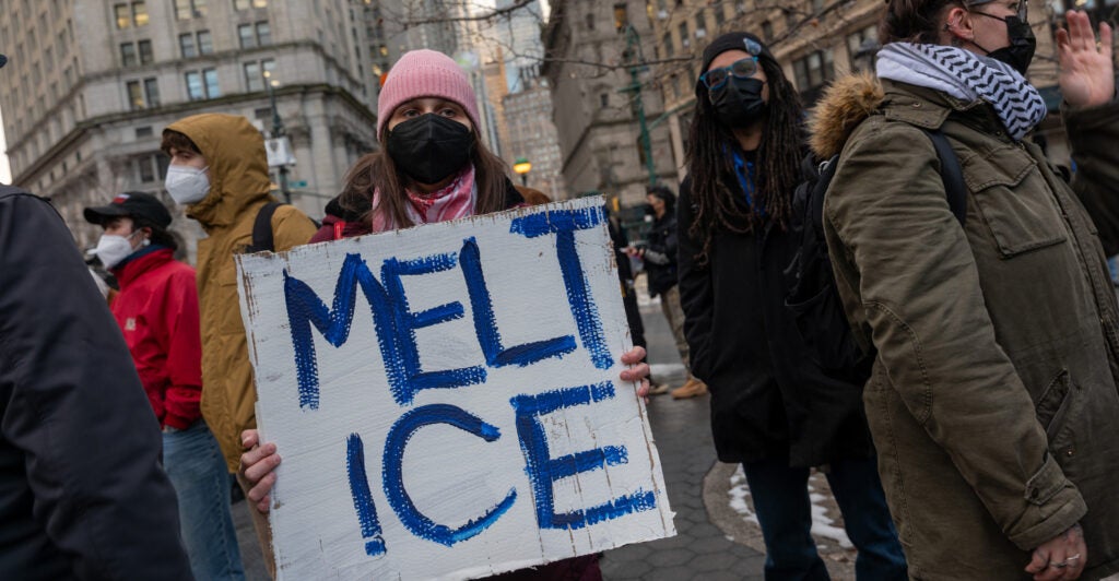 Protesters hold a sign reading "Melt ICE"