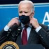 Joe Biden stands and adjusts his mask while talking during a press conference.