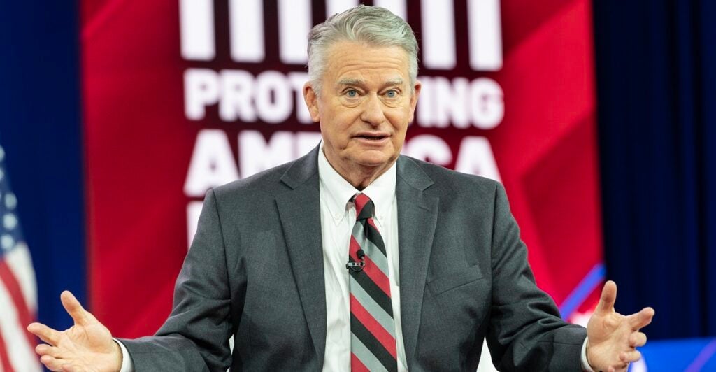 Brad Little stands while his arme are held out.