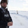 A Royal Canadian mounted police officer standing next to a frozen, snow-covered lake near the U.S. border