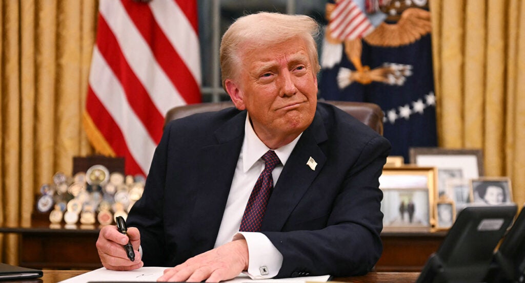 Donald Trump smiles while he signs an executive order