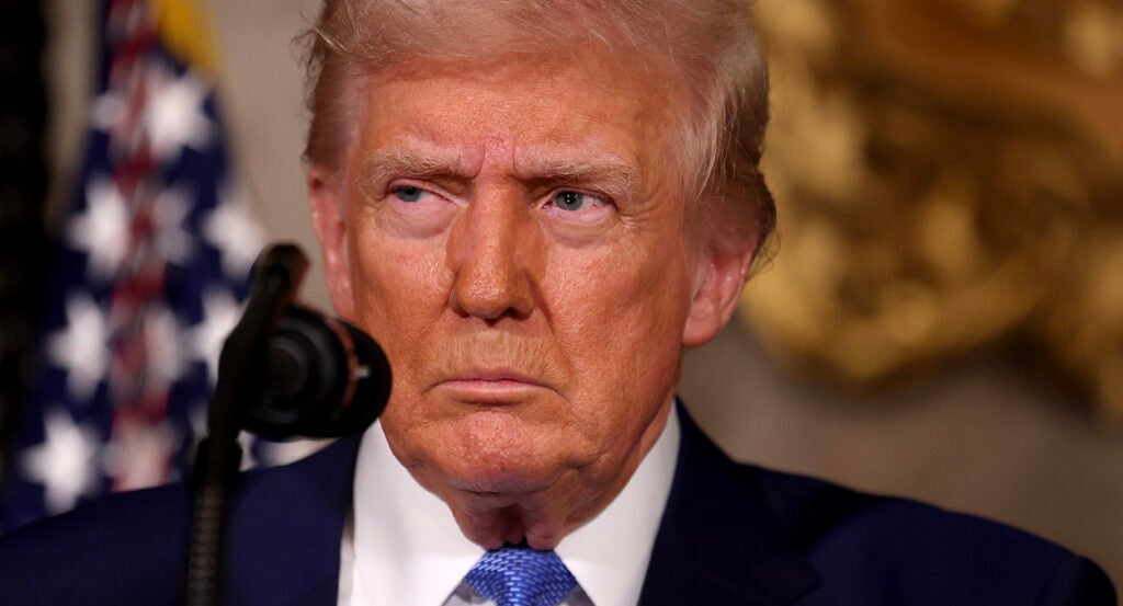 Donald Trump in a blue suit with a blue tie gazes angrily into the distance.