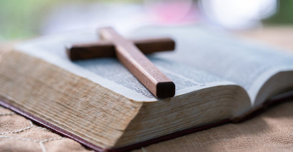 Small wooden cross atop an opened Bible
