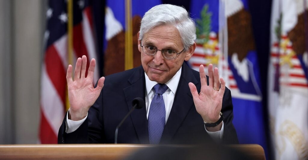 Merrick Garland stands at a podium and puts both his hands up in the halt position during a press conference.
